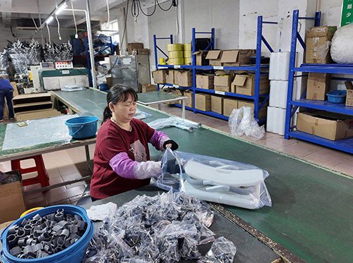A quality control technician at a designated station on the assembly line, using a gauge to verify the critical dimensions of a wheelchair frame component.